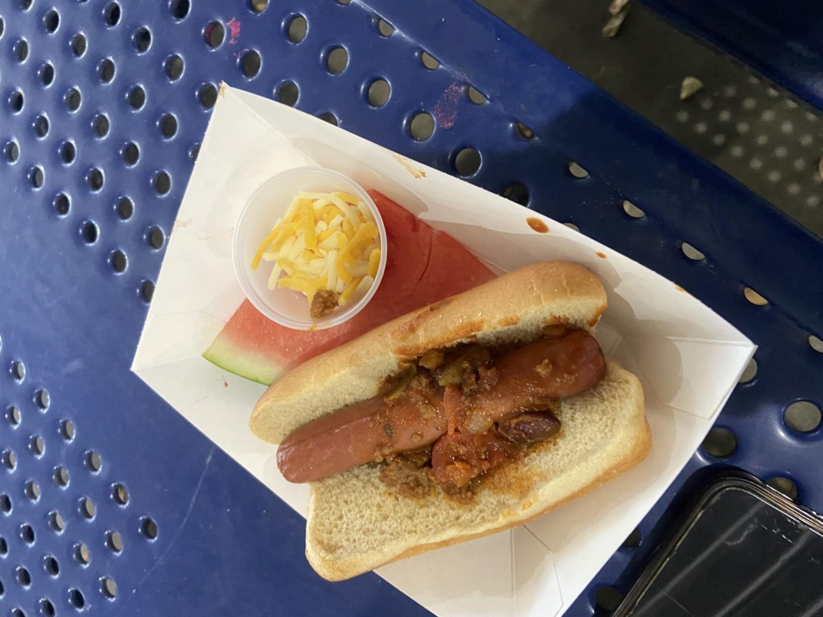 BCCHS Cafeteria chili hot dog with a side of watermelon slice on the bottom with a cup of cheese on top.